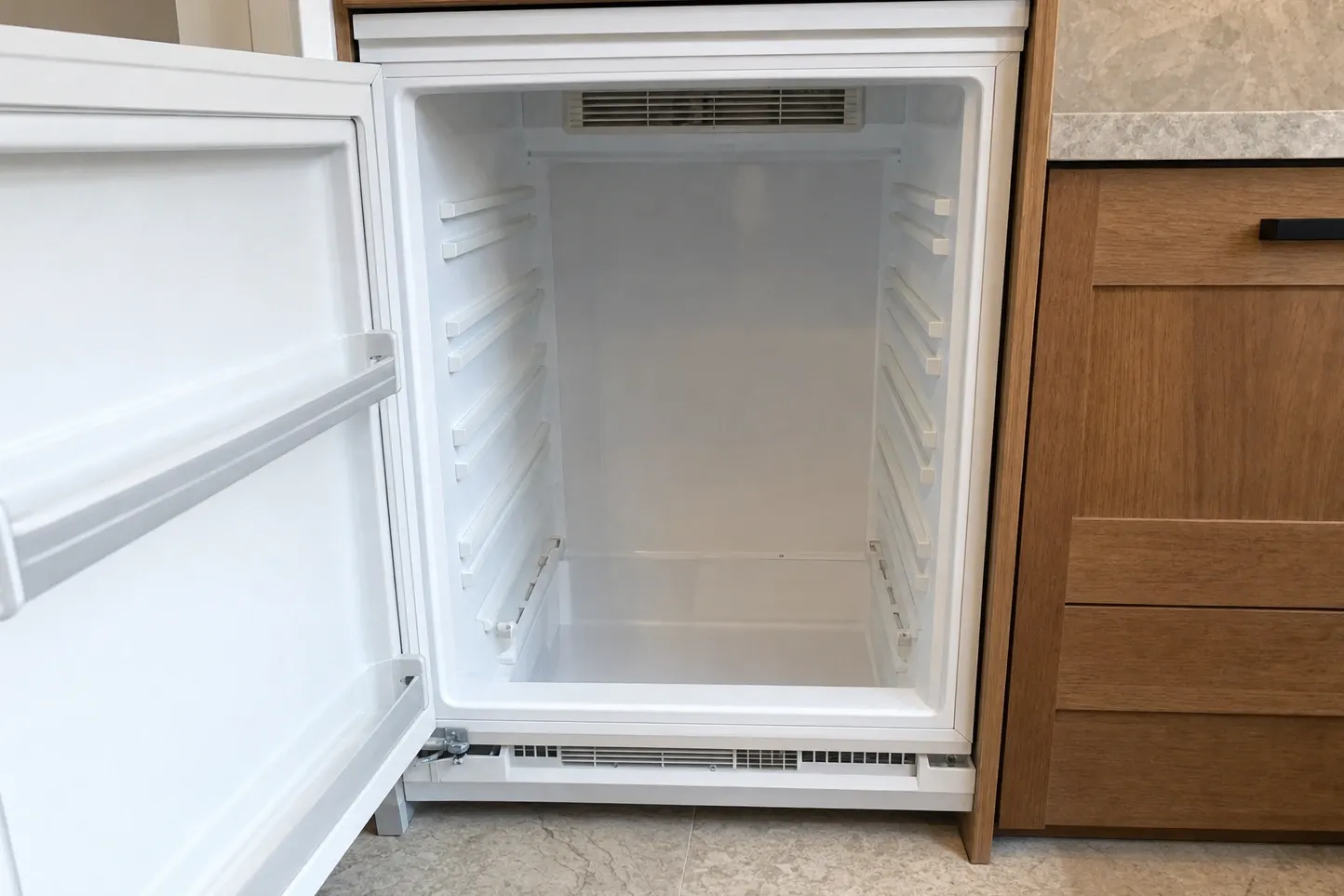 Empty undercounter refrigerator with the door open and the lower kickplate ventilation grille exposed